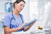 stock photo of computer  - Side view of young female surgeon using digital tablet in front of computer at desk in clinic - JPG 