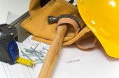 picture of construction worker  - Items used by a construction worker including a leather tool belt a hammer a tape measure tools floor plans and a yellow hard hat - JPG 