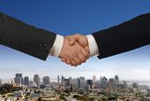 picture of handshake  - Two businessmen shaking hands with daytime city skyline in the background - JPG 