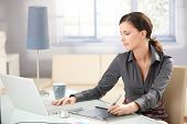stock photo of working  - Young graphic designer working on laptop using tablet at home - JPG 
