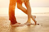 A young  loving  couple hugging and kissing on the beach at sunset. Two lovers, man and woman barefoot near the water. Summer in love 