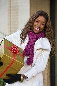 pic of africanamerican  - Attractive young happy woman walking in an urban city environment and holding a Christmas gift wrapped in gold paper - JPG 