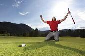 picture of golf  - Professional young male golf player on knees and arms raised with putter in hand on golf green being overjoyed as golf ball drops into cup - JPG 