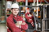 image of industrial  - young smiling warehouse worker driver in uniform in front of forklift stacker loader - JPG 
