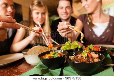 Picture or Photo of Young people eating in a Thai restaurant; they eating with chopsticks