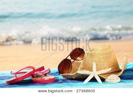Picture or Photo of Summer straw hat with towel,sunglasses and flip flops on sandy beach