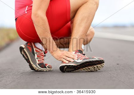 Picture or Photo of Broken twisted ankle - running sport injury. Male runner touching foot in pain due to sprained ankle.