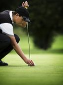 foto of golf  - Young golf player squatting to put down ball at green - JPG 