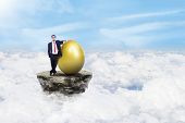 picture of finance  - Businessman is standing beside a golden egg above the clouds - JPG 