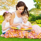 foto of outdoor  - Image of cute young female with two little children read book outdoors - JPG 