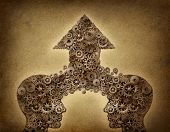 stock photo of merger  - Business cooperation success teamwork growth concept with two human head shapes merging together to form an upward arrow made of gears and cogs as a financial symbol on a grunge old parchment paper - JPG 