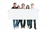 stock photo of group  - Happy young group of people standing together and holding a blank sign for your text - JPG 