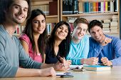 stock photo of group  - Happy group of young students studying together in a college library and looking at camera smiling - JPG 