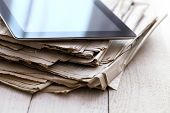 picture of portable  - Stack of old newspapers and a tablet pc on the wooden table - JPG 