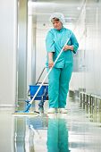 stock photo of pass  - Adult cleaner maid woman with mop and uniform cleaning corridor pass floor of pharmacy industry factory or clinic - JPG 