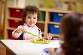 pic of preschool  - Caucasian and hispanic female preschoolers eating pasta and smiling - JPG 