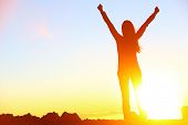 stock photo of sunset  - Happy celebrating winning success woman at sunset or sunrise standing elated with arms raised up above her head in celebration of having reached mountain top summit goal during hiking travel trek - JPG 