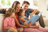 stock photo of thirties  - Parents Sitting With Children Reading Story Indoors - JPG 