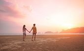 stock photo of beach  - Young couple walking on a tropical beach at sunset - JPG 