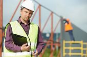 foto of construction  - site manager builder worker in uniform and safety protective equipment at construction site in front of metal construction frames - JPG 