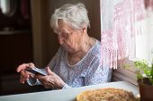 An elderly woman sits with a smartphone in her hands.