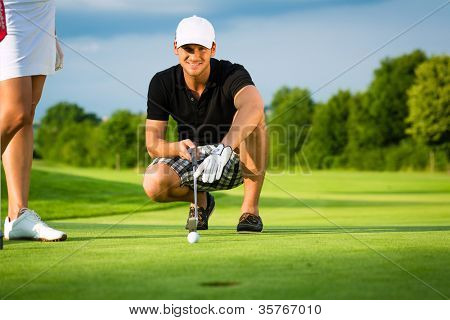 Picture or Photo of Young golf player on course putting, he aiming for his put shot