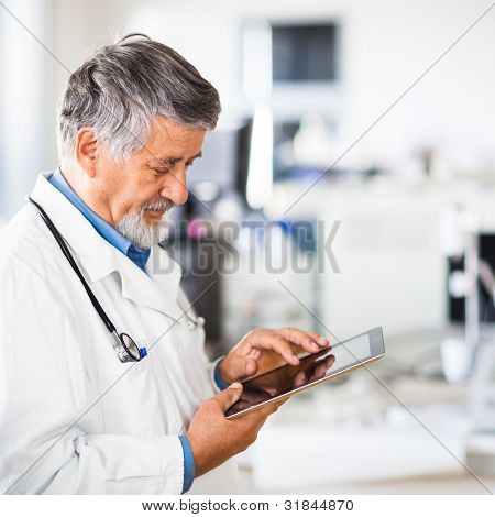 Picture or Photo of Senior doctor using his tablet computer at work (color toned image)