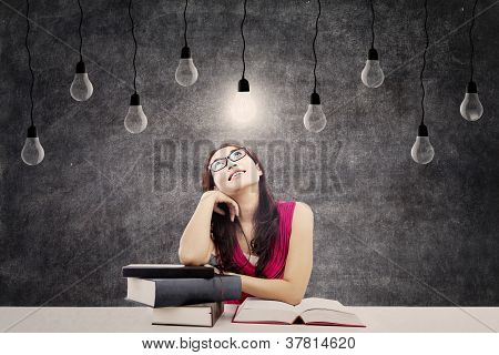 Picture or Photo of Portrait of smart female college student with books and bright light bulb above her head as a symbol of bright ideas