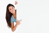 stock photo of woman  - Smiling woman pointing at a board while standing against a white background - JPG 