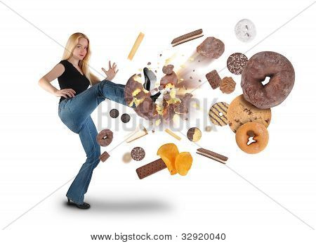 Picture or Photo of A young woman is kicking donuts on a white background within an assortment of junk food. There are cookies, chips and ice cream. Use it for a diet or nutrition concept.