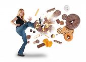 stock photo of health  - A young woman is kicking donuts on a white background within an assortment of junk food - JPG 