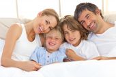 stock photo of family  - Happy family reading a book lying in bed - JPG 